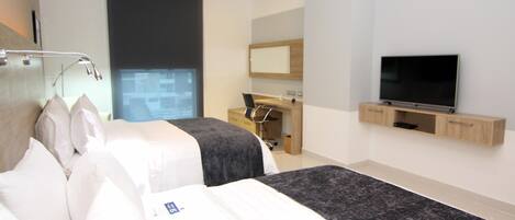 A modern hotel room with a large bed, a desk, a television, and a window with a view.