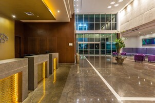 Un vestíbulo moderno con un mostrador de recepción, una planta grande y asientos morados.