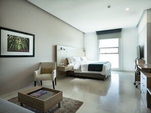 A modern bedroom with a bed, bedside tables, a chair, a desk, and a large window. - Hotel Sky Collection Barranquilla (Barranquilla)