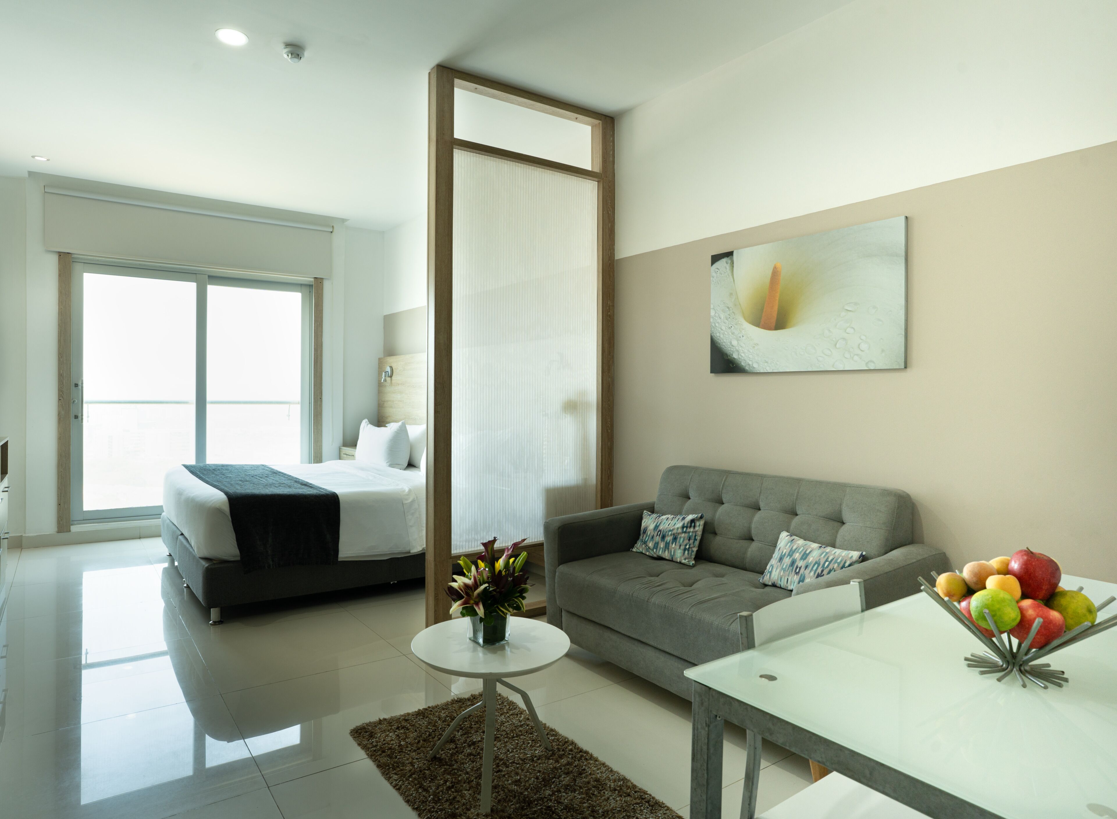 Une chambre d’hôtel moderne équipée d’un lit, d’un canapé et d’un coin repas agrémenté d’un panier de fruits.