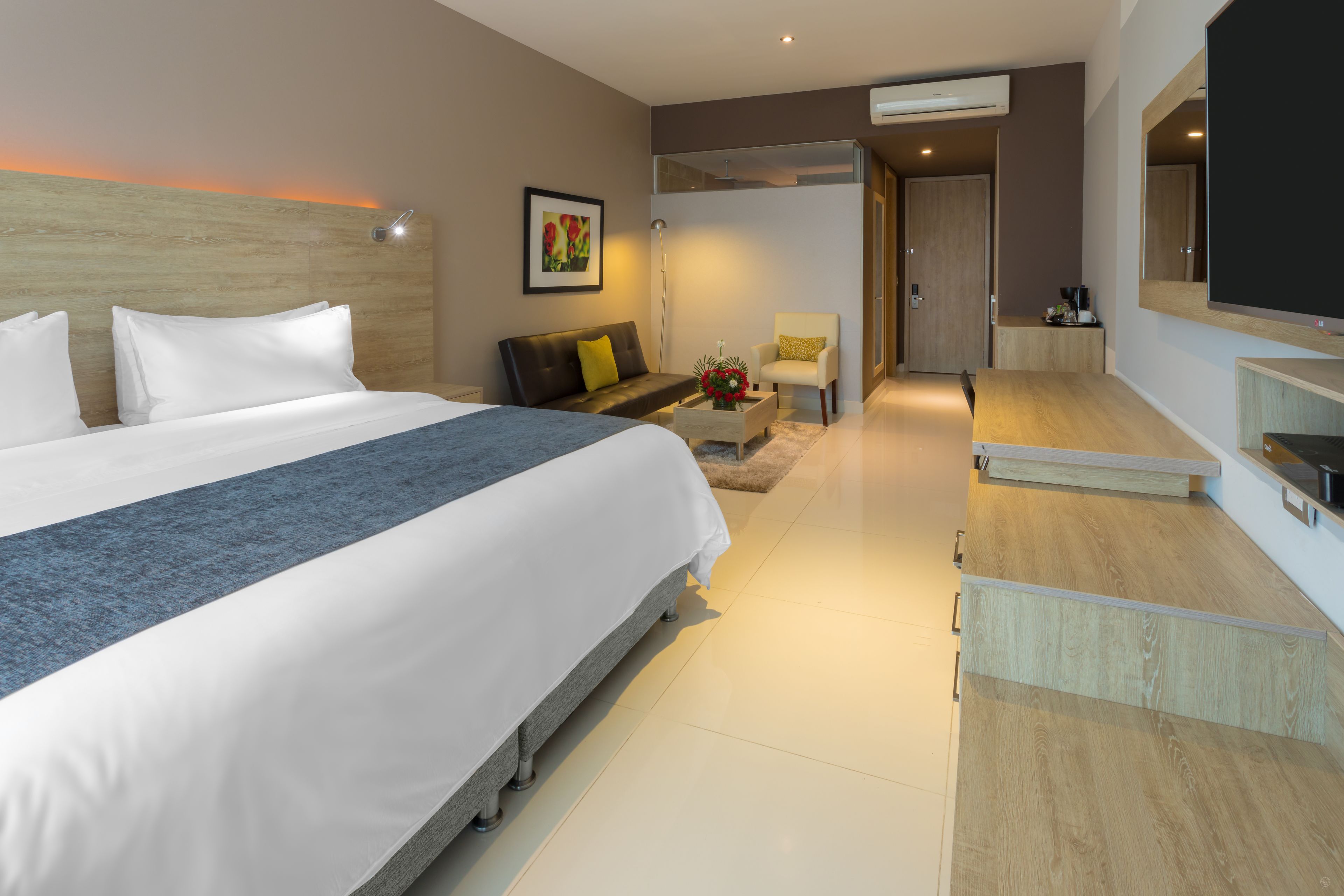 Une chambre d’hôtel moderne avec un grand lit, un canapé, une petite table agrémentée de fleurs, une télévision et un bureau avec un ordinateur.