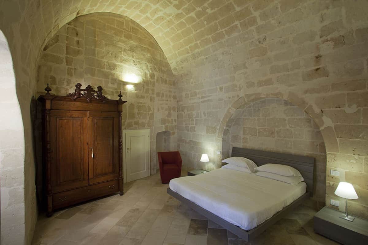 Een slaapkamer met een stenen muur, een houten garderobe, een bed en twee bedlampen.
