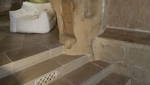 Un intérieur en pierre avec un banc rembourré de couleur blanche, une lampe et un mur en pierre percé de trous.