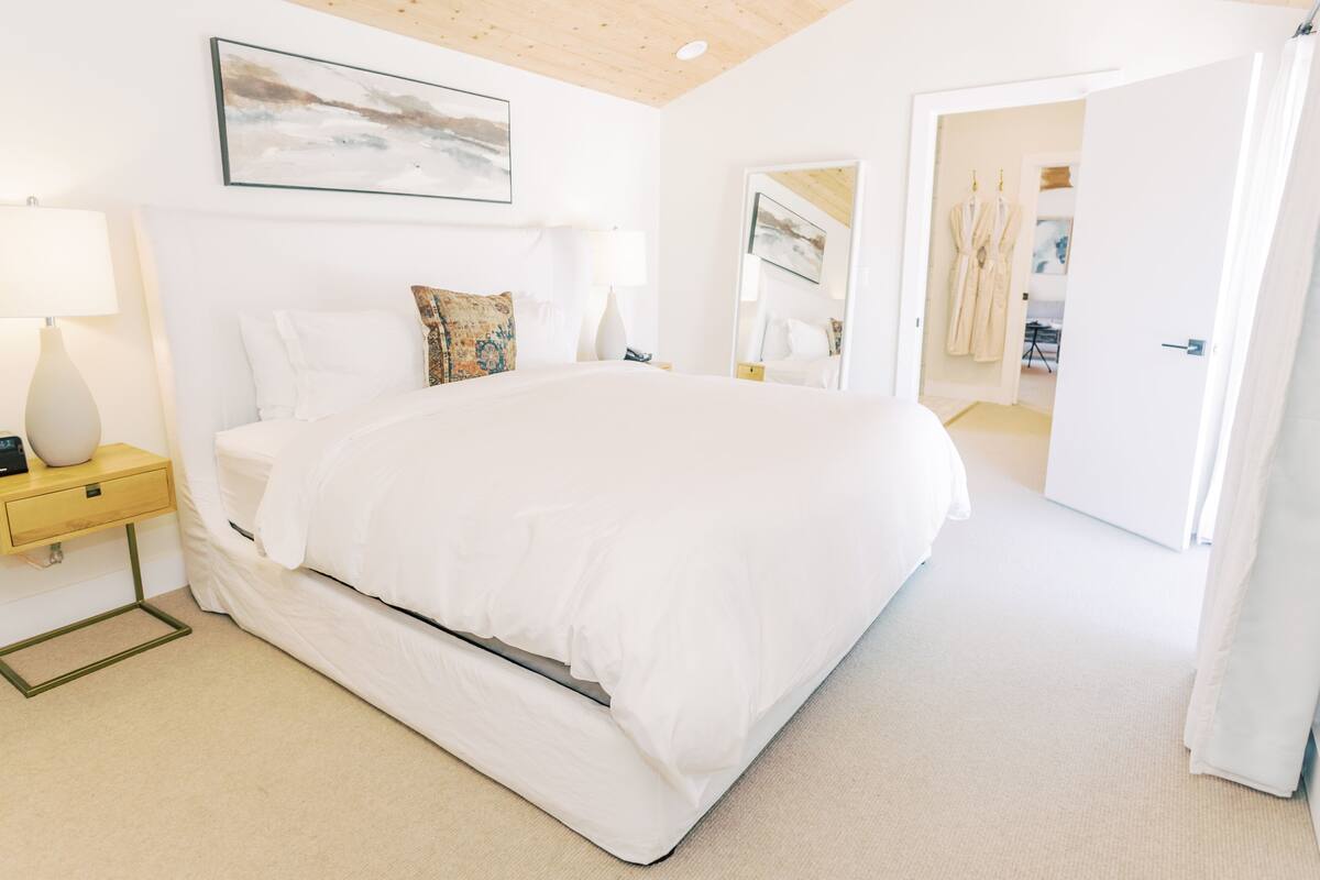 A spacious bedroom with a large bed, a bedside table with a lamp, and a door leading to a bathroom.