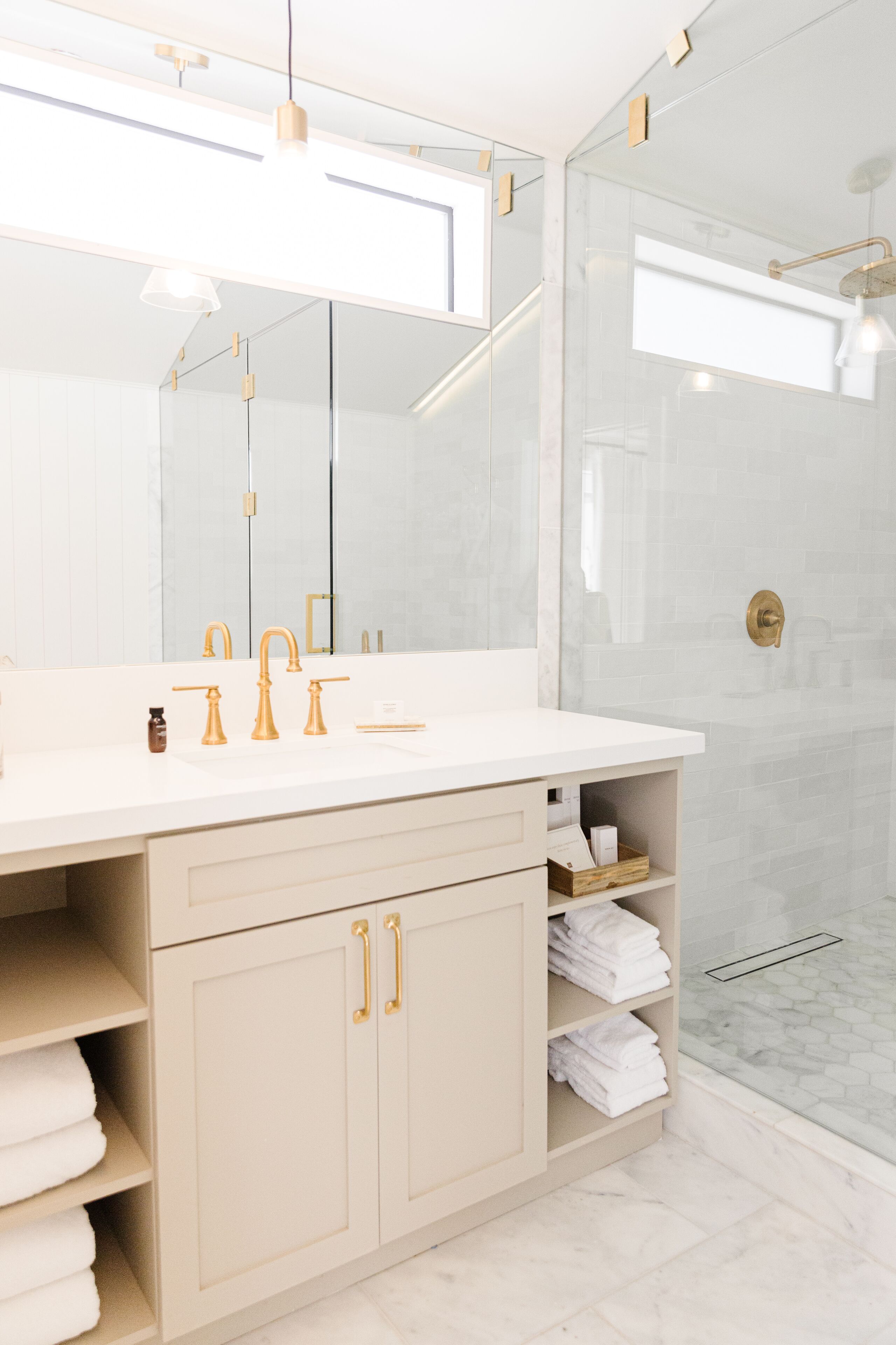 Un baño moderno con tocador blanco, detalles dorados y cabina de ducha de vidrio.