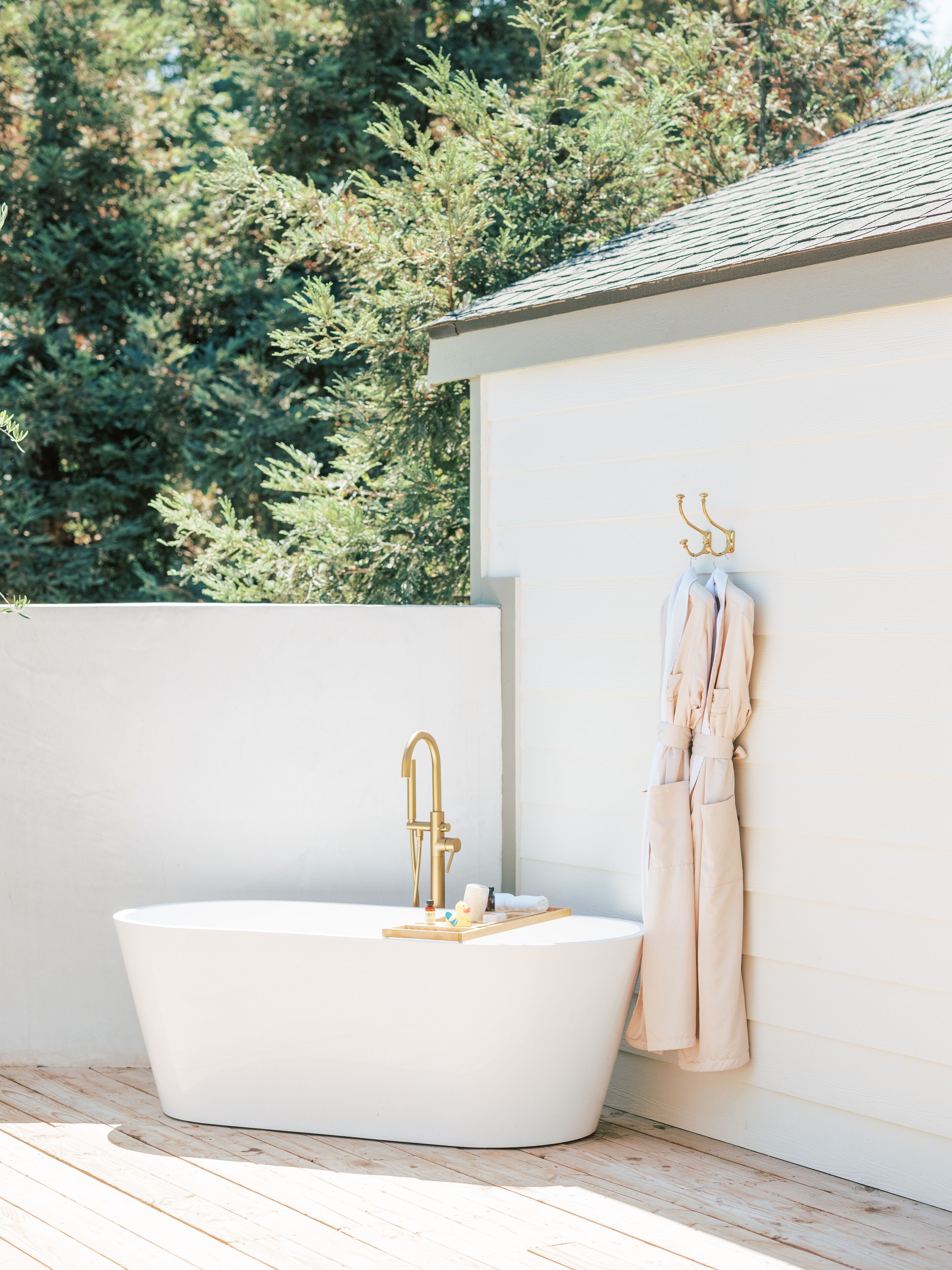 Une salle de bain extérieure moderne avec une baignoire sur pied, un robinet doré et un porte-serviettes adossé à un mur blanc.