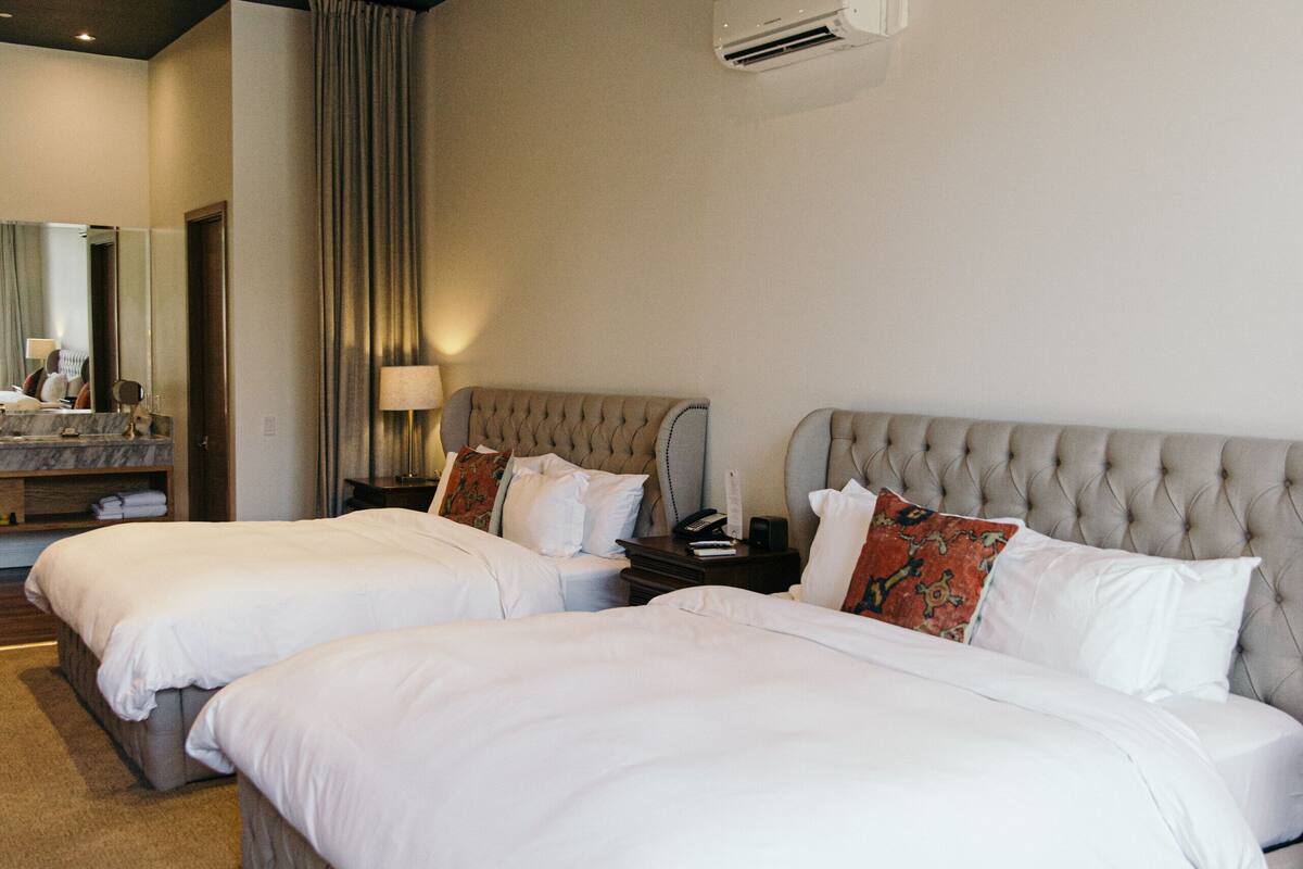 A hotel room with two beds, a large mirror, a vanity with a sink, and an air conditioning unit on the wall.