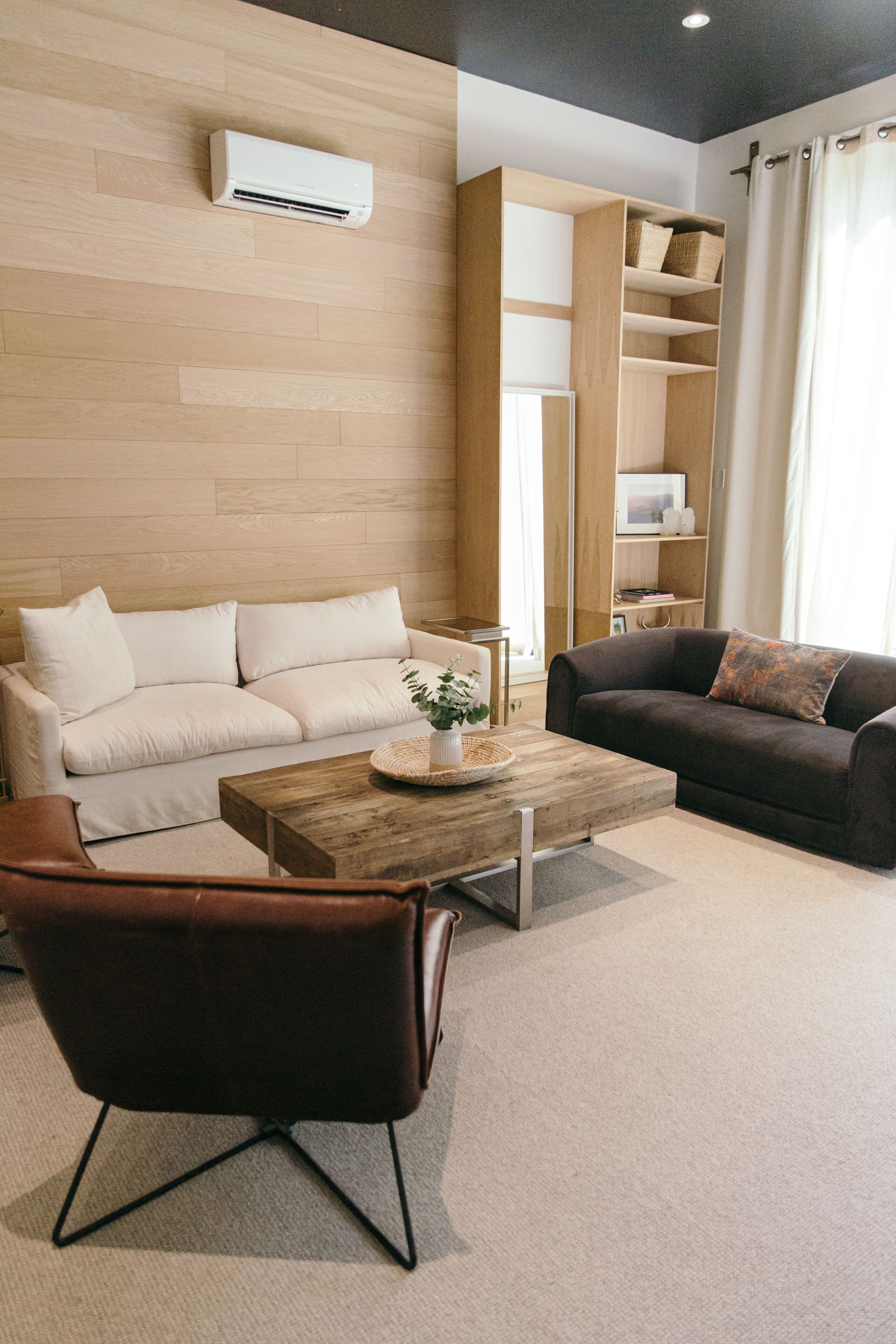 A modern living room with a beige sofa, a dark brown sofa, a wooden coffee table, and a leather armchair.