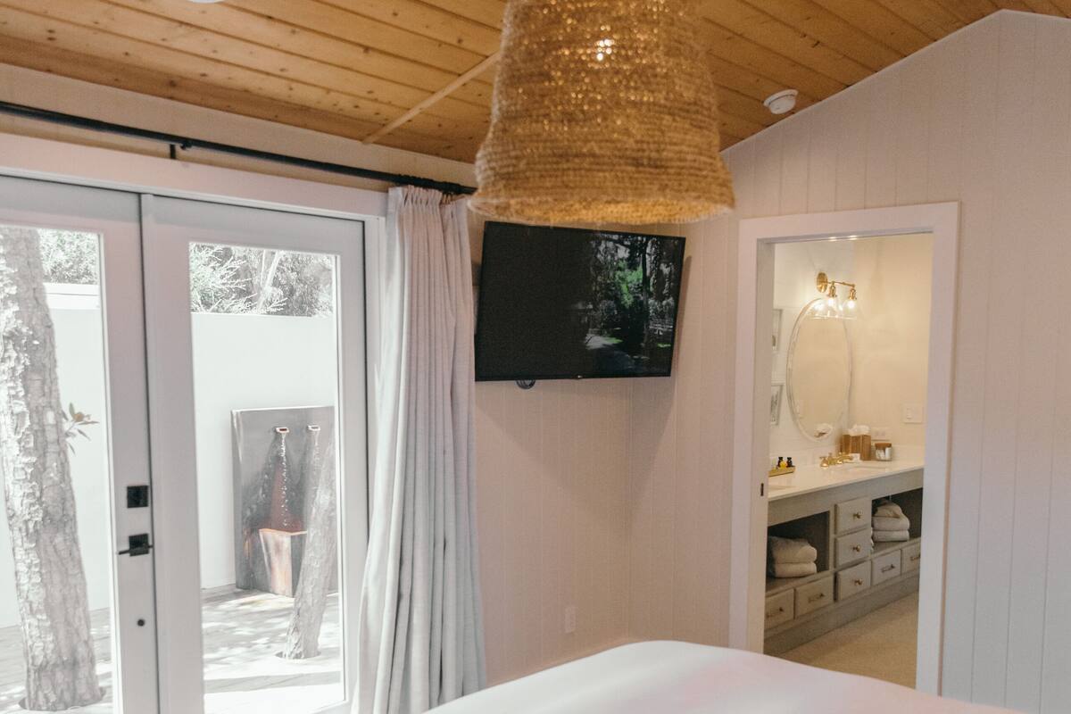 A bedroom with a large bed, a television mounted on the wall, and a wooden ceiling.