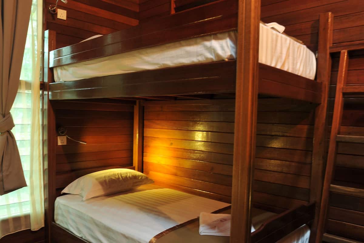 Une chambre avec des lits superposés, des murs et des planchers en bois, une fenêtre avec des rideaux et une table de chevet avec une lampe.