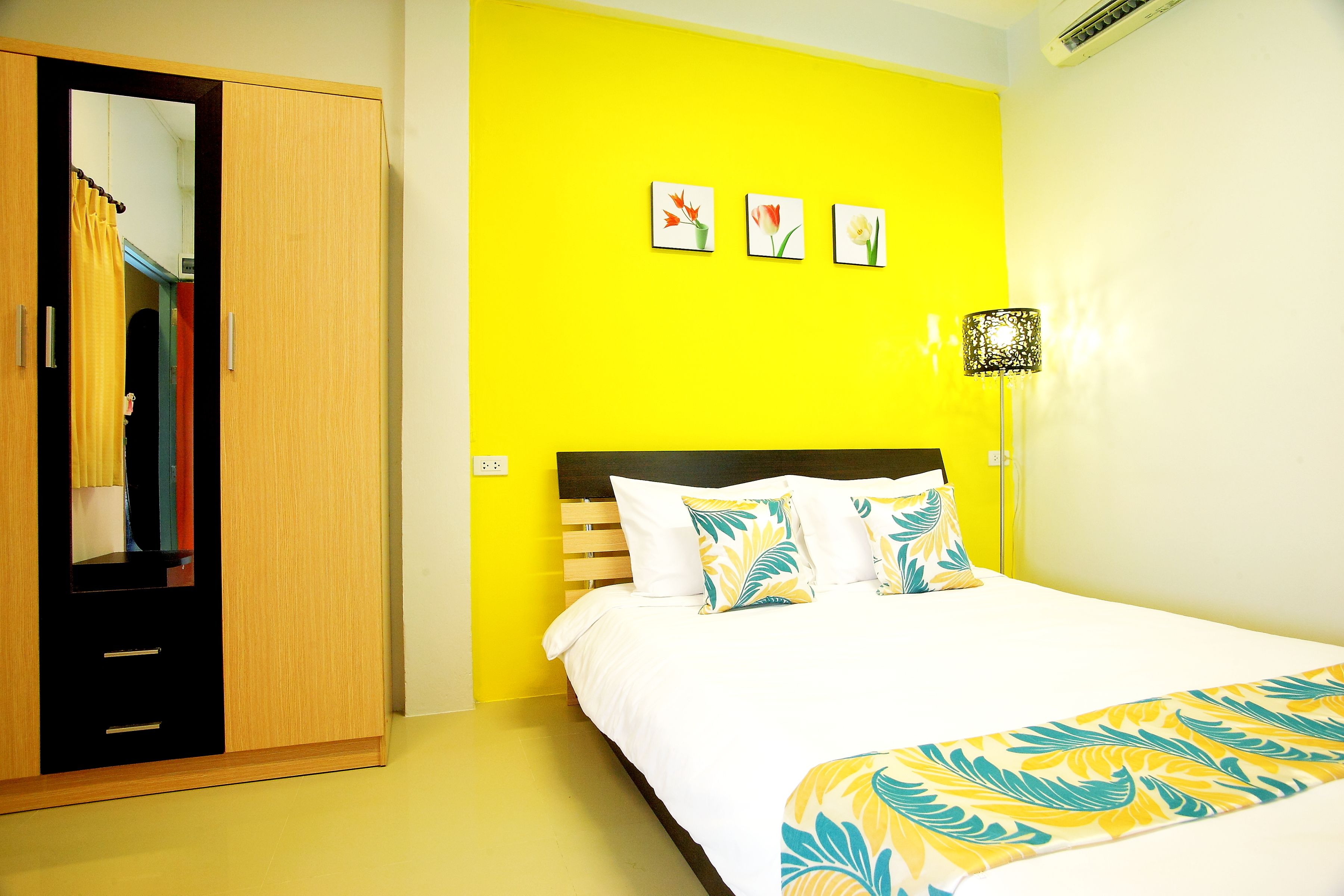 A room with a bed, a wardrobe, and a bright yellow wall.