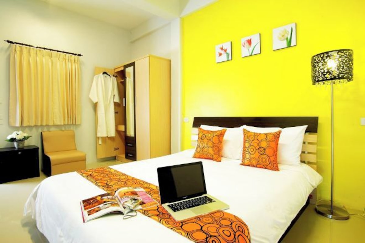 A hotel room with a bed, a laptop, a magazine, and a lamp.