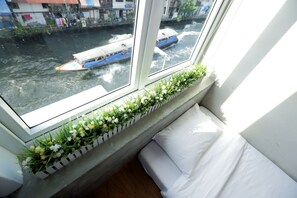 A window with a view of a canal, a boat, and a flower box on the sill. - Smile Inn (Bangkok)