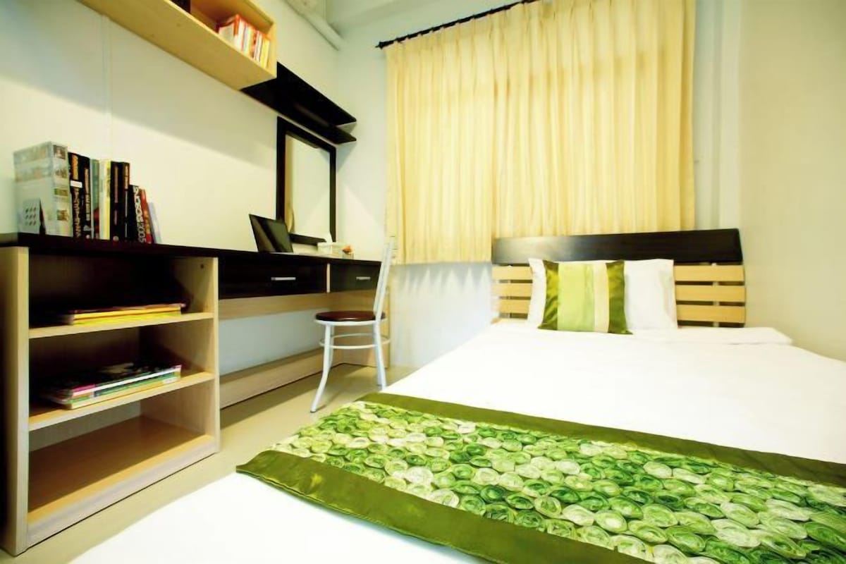 A neatly arranged bedroom with a bed, a desk, and a bookshelf.
