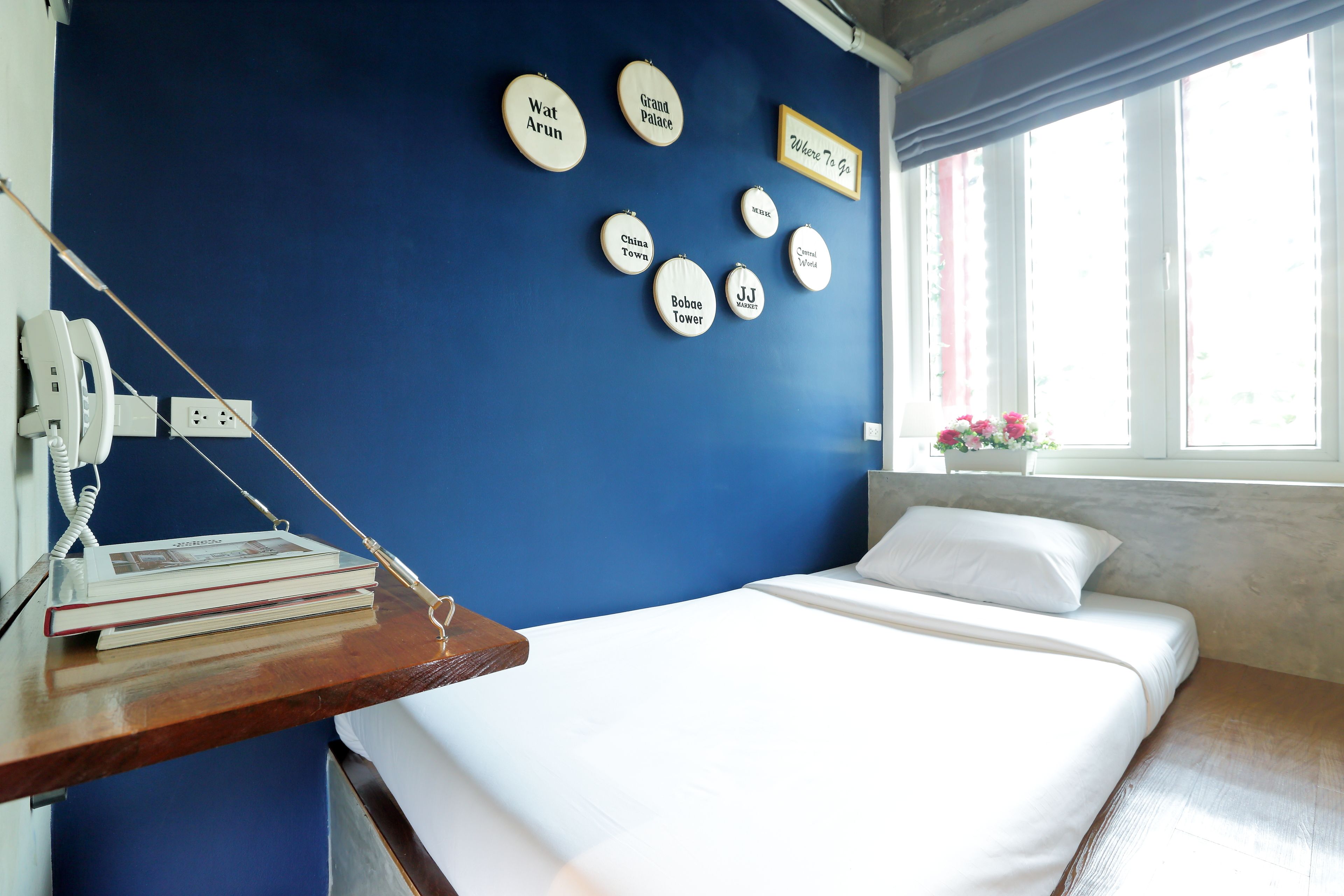 A bedroom with a blue wall, a bed with white bedding, a bedside table with a lamp, and a window with curtains.