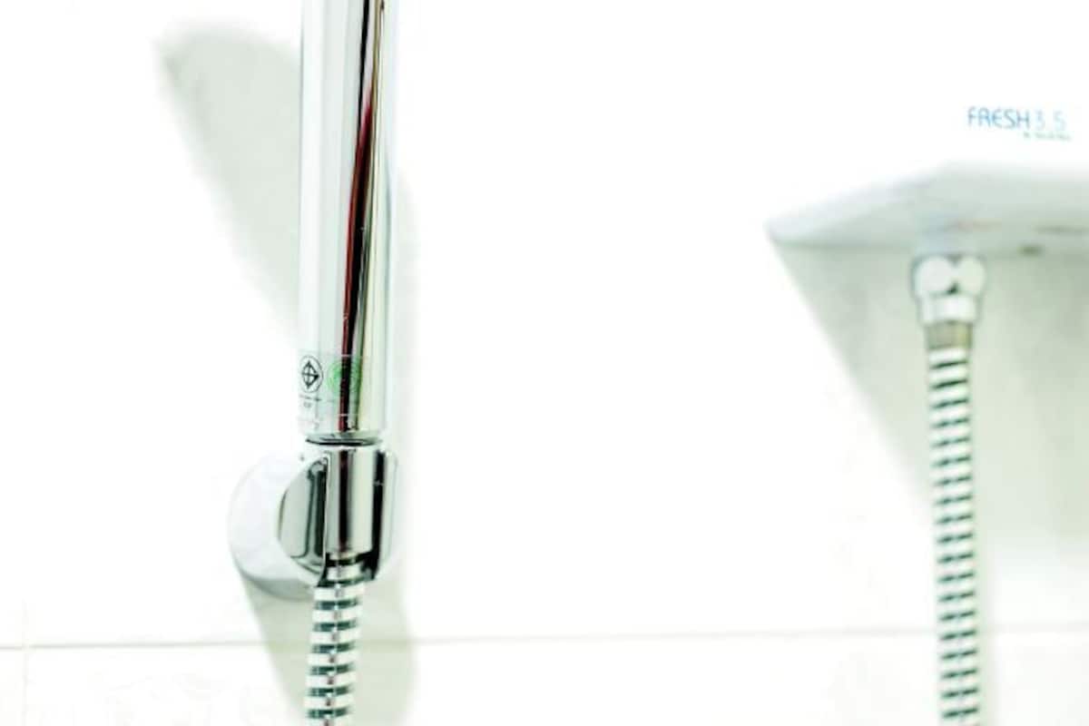 A chrome showerhead with a flexible hose, mounted on a white wall.