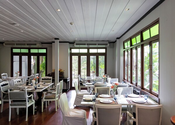 Un comedor con mesas dispuestas para el servicio, ventanas amplias con vistas a zonas verdes e iluminación empotrada en el techo.
