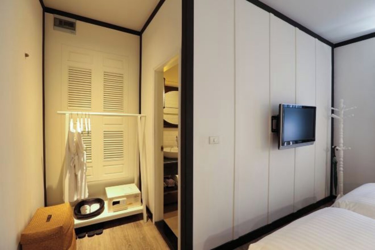 A hotel room with a bed, a television mounted on the wall, a closet with sliding doors, and a small stool.
