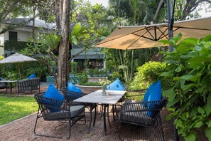An outdoor patio with wicker furniture, a table, and a large umbrella. - The Raweekanlaya Hotel Bangkok (Bangkok)