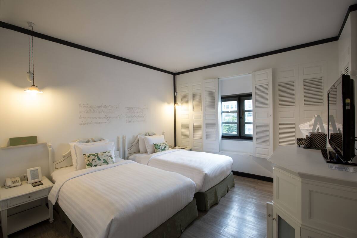 Une chambre d’hôtel avec deux lits, un bureau avec un téléphone et une fenêtre avec des volets.