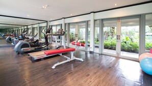 A gym with exercise equipment, large windows, and a view of greenery. - The Raweekanlaya Hotel Bangkok (Bangkok)