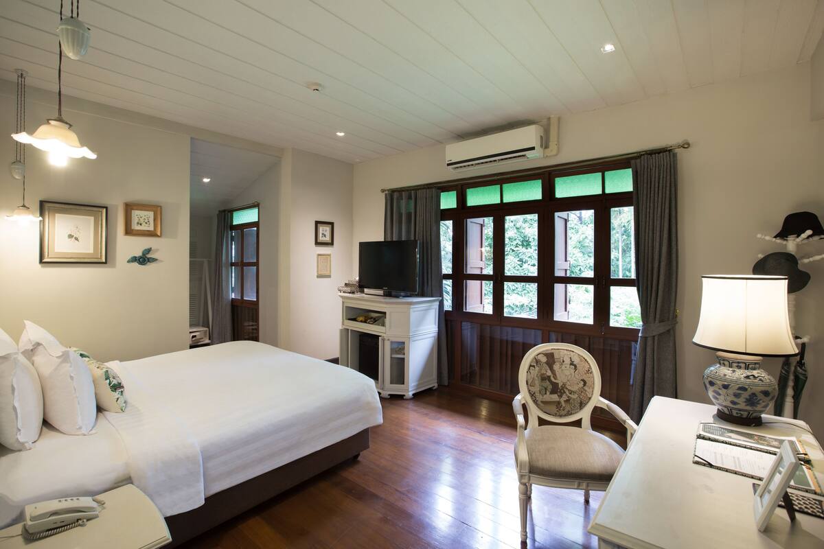 Une chambre d’hôtel avec un lit, un bureau avec une lampe, une chaise, un téléviseur et une fenêtre avec des rideaux.