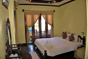 A hotel room with a large bed, a wooden headboard, a small table, and a view of the outside through a door. - Visoun Namsok Hotel (Luang Prabang)