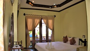 A bedroom with a large bed, a wooden headboard, and a view through the window. - Visoun Namsok Hotel (Luang Prabang)