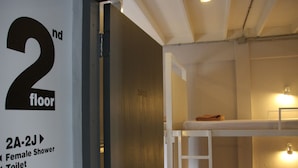 A hotel room with a bunk bed, a wooden door, and a sign indicating the room number and amenities. - Bangkok Nomad Hostel (Bangkok)