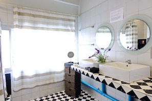 A bathroom with two sinks, a mirror, a window with a striped curtain, and a checkered floor. - Bangkok Nomad Hostel (Bangkok)