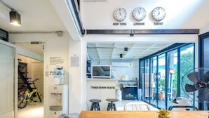 A modern hostel interior with a wooden dining table, chairs, a fan, and a sign indicating the hostel's name. - Bangkok Nomad Hostel (Bangkok)