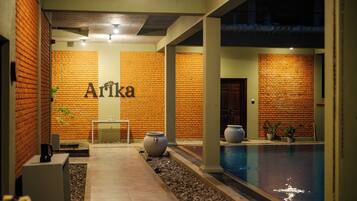 A hotel lobby with a brick wall, a pool, and a reception desk.