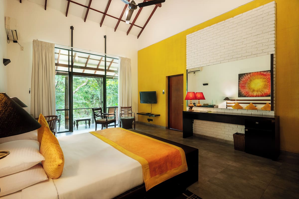 A hotel room with a bed, a desk with a computer, a TV, and a balcony with chairs.