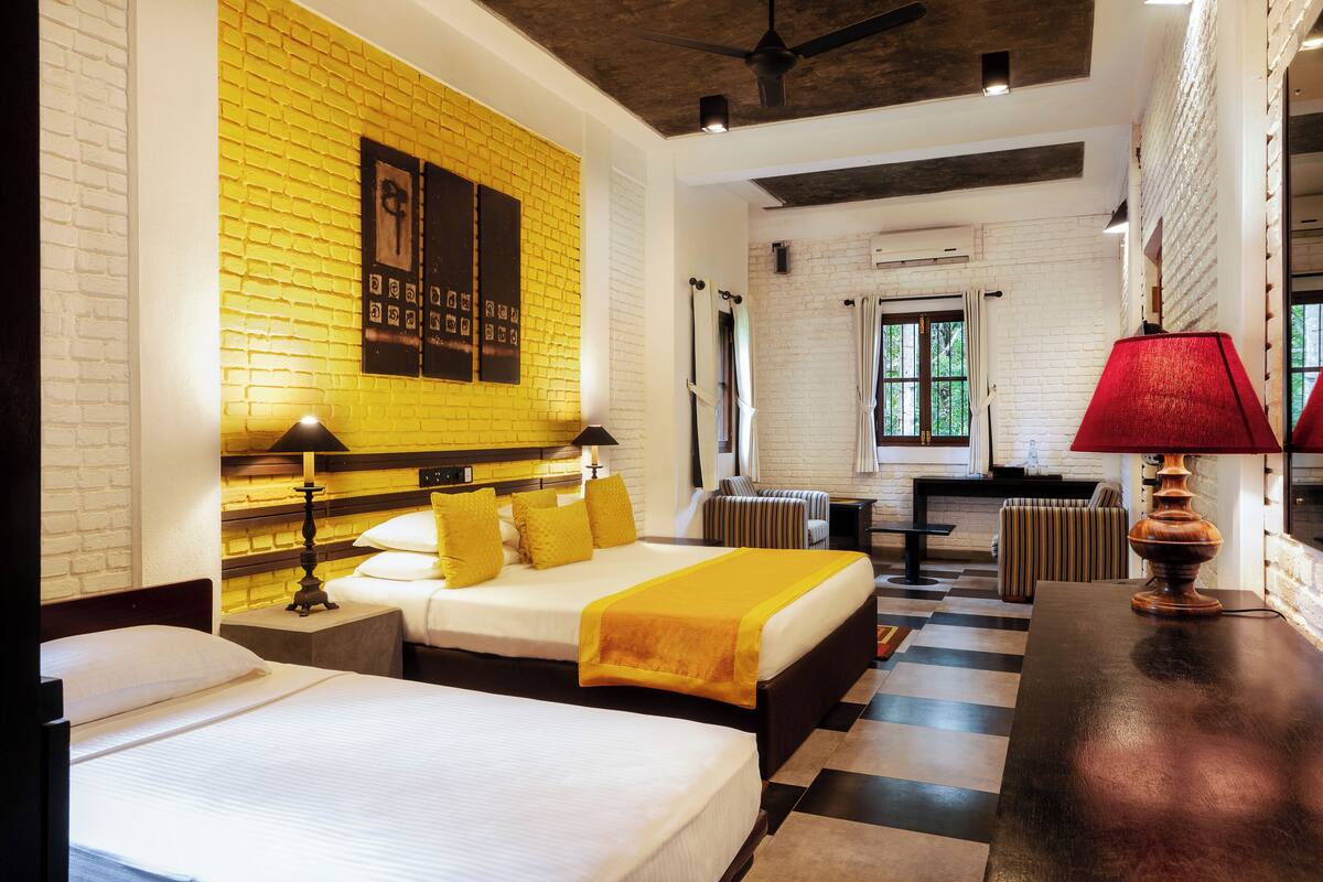 A hotel room with a brick wall, two beds, a red lamp, and a view of the outdoors.