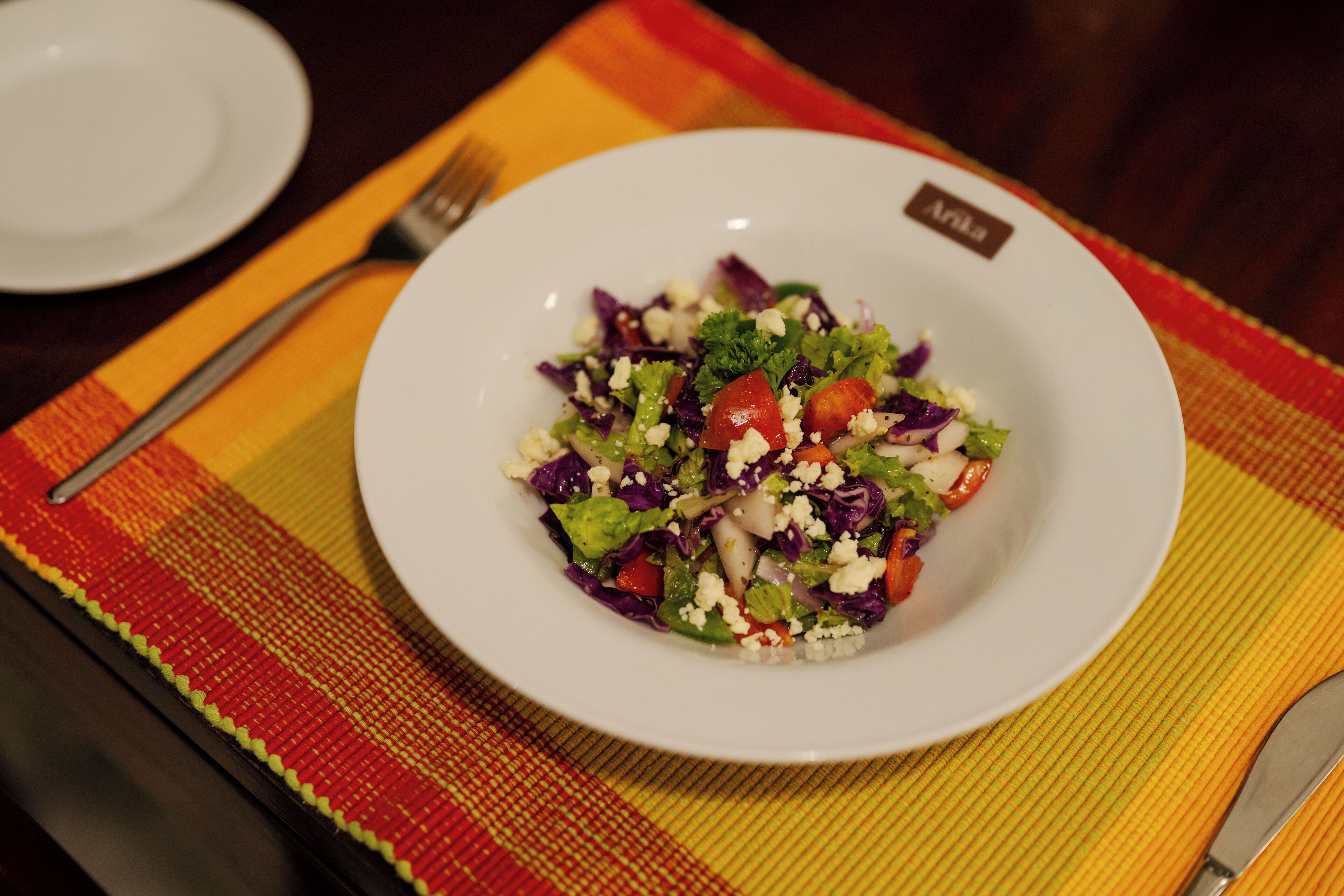 A white plate with a salad on a colorful placemat.