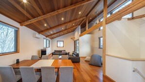 A spacious room with a wooden ceiling, a large dining table with chairs, a sofa, and a patterned armchair. - Bluebird Chalets (Hakuba)