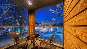 A cozy room with a large window overlooking a snowy landscape, a wooden interior, and a round table with chairs. - Bluebird Chalets (Hakuba)