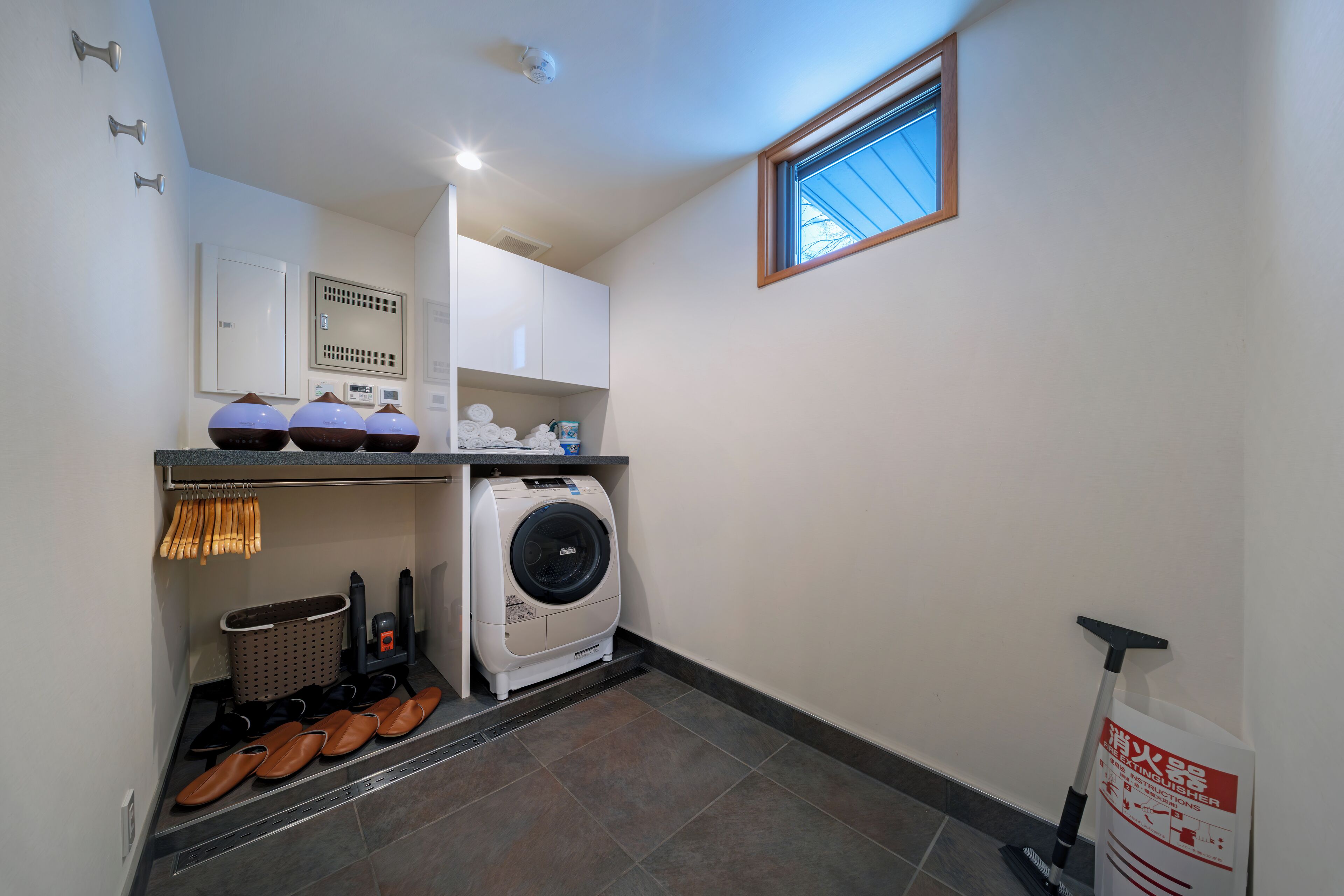 A laundry room with a washing machine, drying rack, and shoe rack.