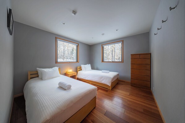Un dormitorio con dos camas, suelo de madera y ventanas amplias.