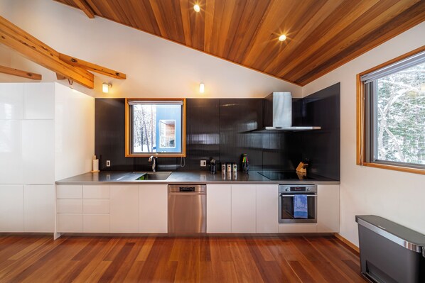 A modern kitchen with wooden ceiling beams, built-in appliances, and a large window providing natural light. - Bluebird Chalets (Hakuba)