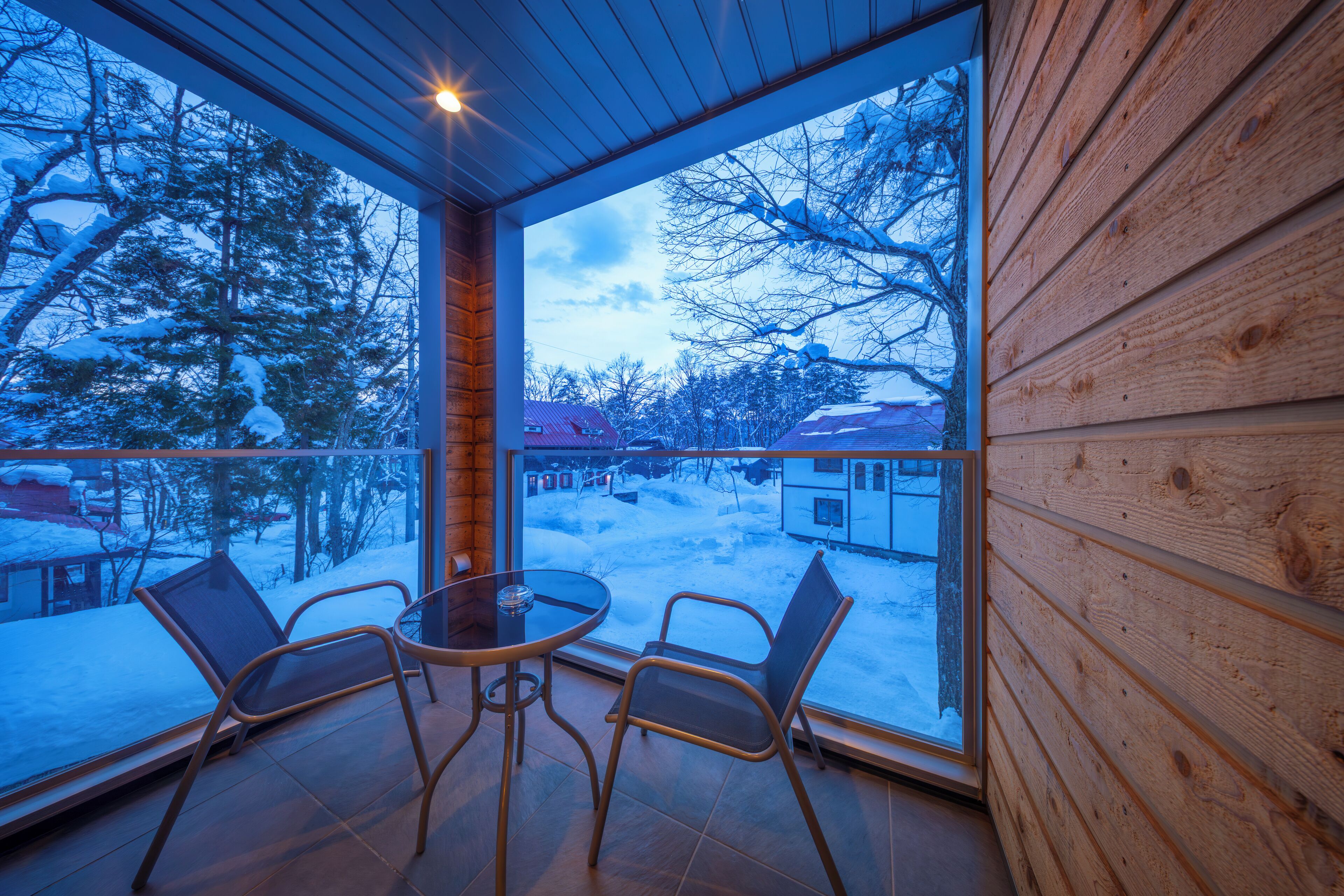 A cozy wooden cabin with a glass dining area overlooking a snowy landscape.