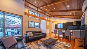 A spacious living area with a black leather sofa, a wooden coffee table, and a large window offering a view of a snowy landscape. - Bluebird Chalets (Hakuba)