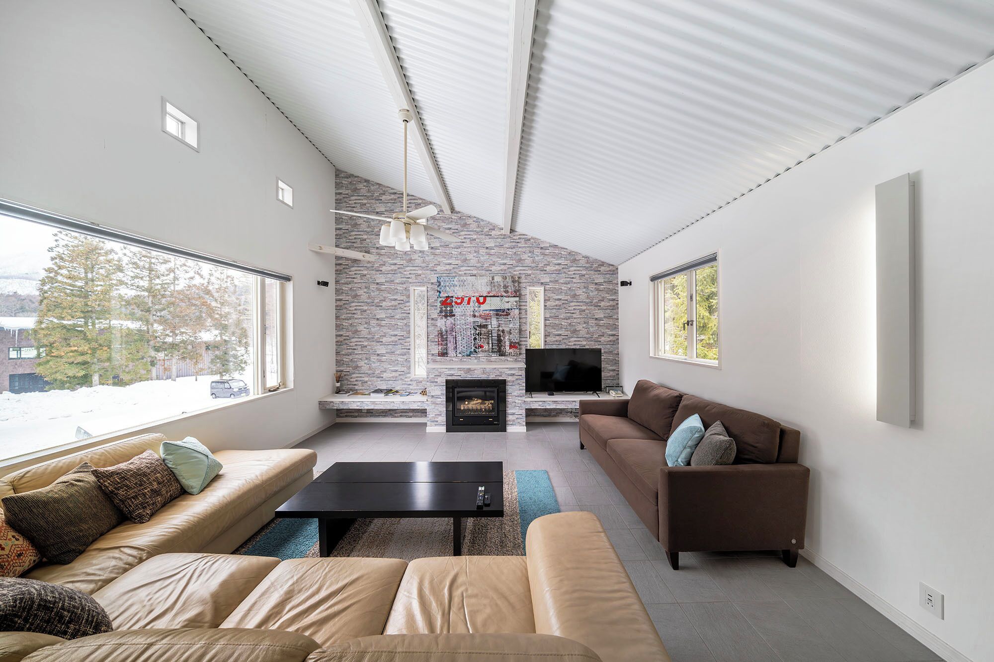 A modern living room with a stone fireplace, a flat-screen TV, and a brown leather sofa.