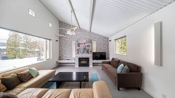 A modern living room with a stone fireplace, a flat-screen TV, and a brown leather sofa.