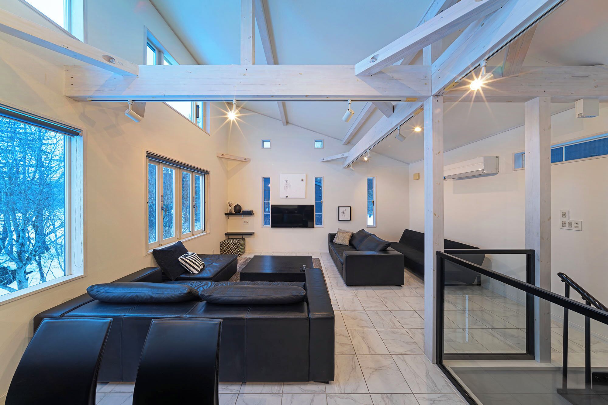 A modern living room with a sectional sofa, a flat-screen TV, and large windows.