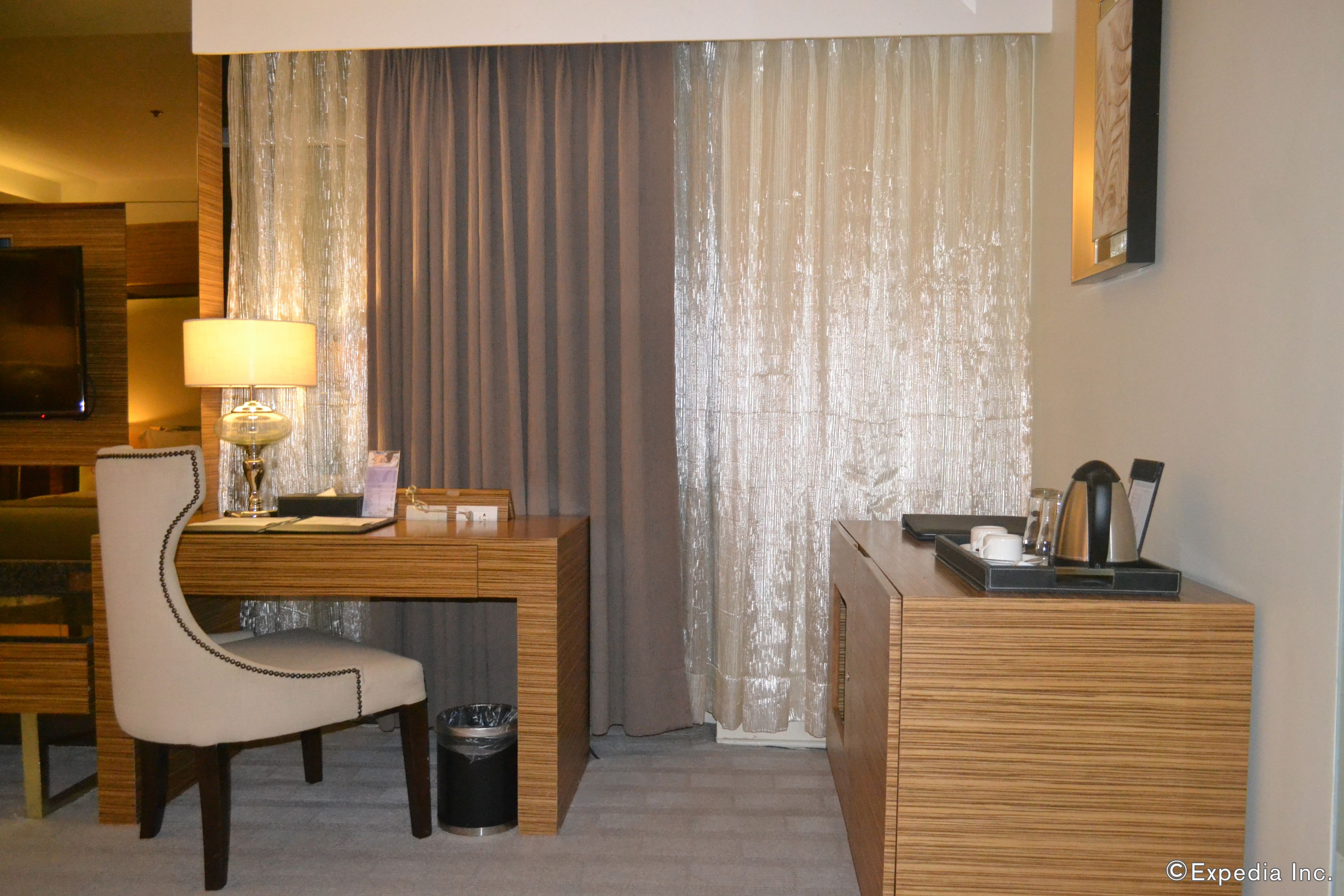Una habitación de hotel con un escritorio de madera, una silla, una lámpara, un cubo de basura y un minibar.