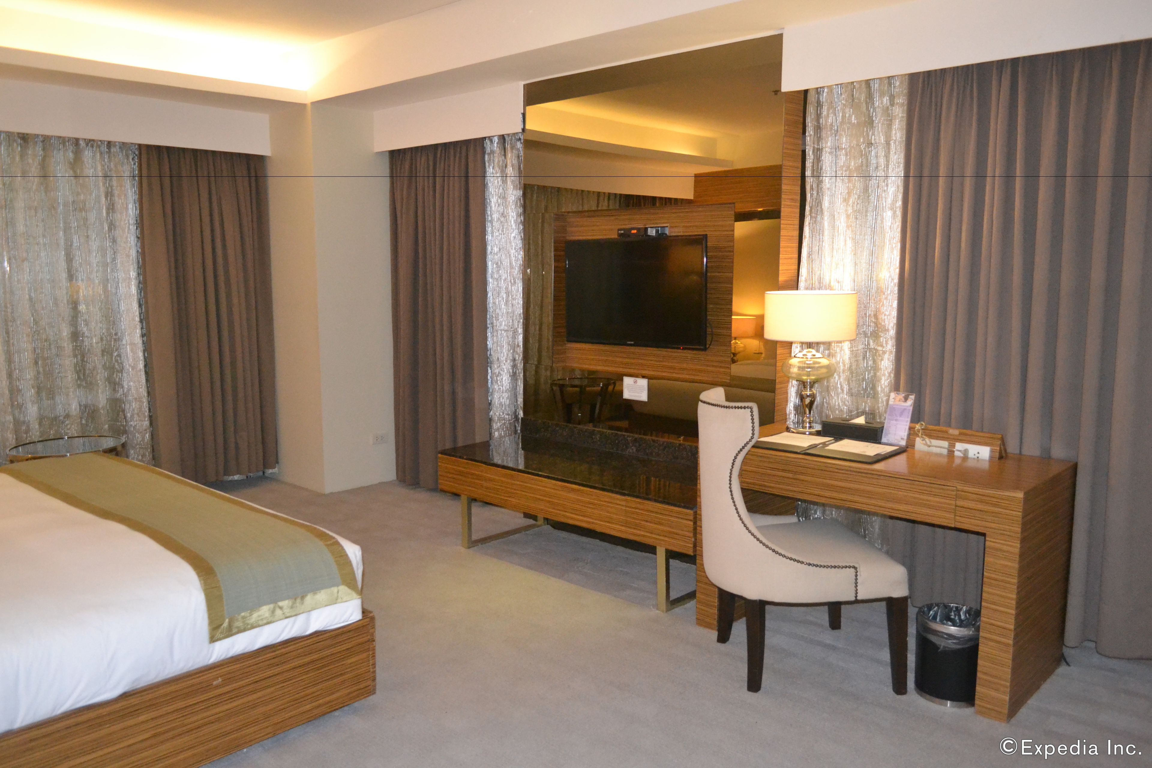A hotel room with a bed, a desk with a chair, a television, and a lamp.