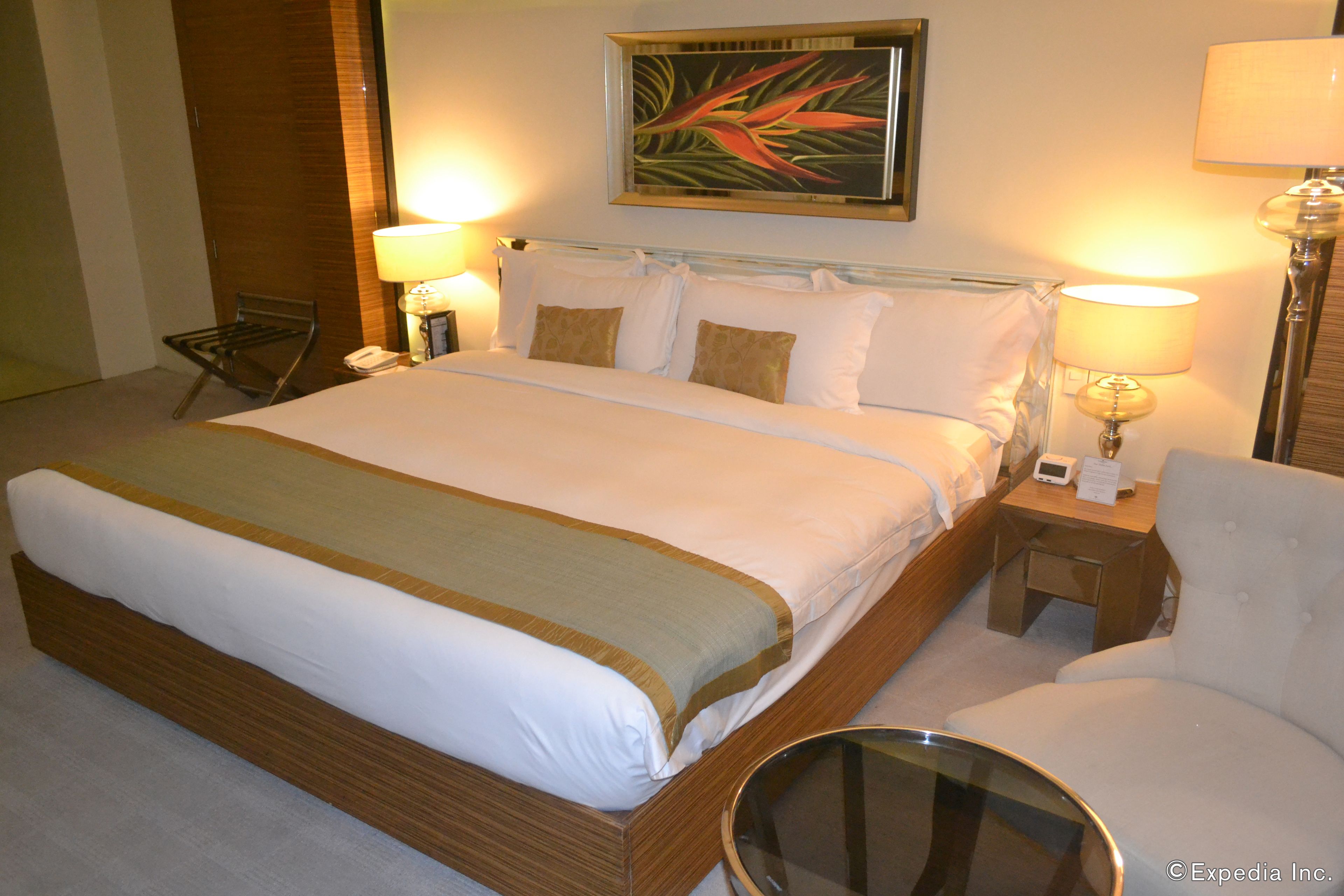 A hotel room with a large bed, two bedside tables, a chair, a desk, and a painting on the wall.