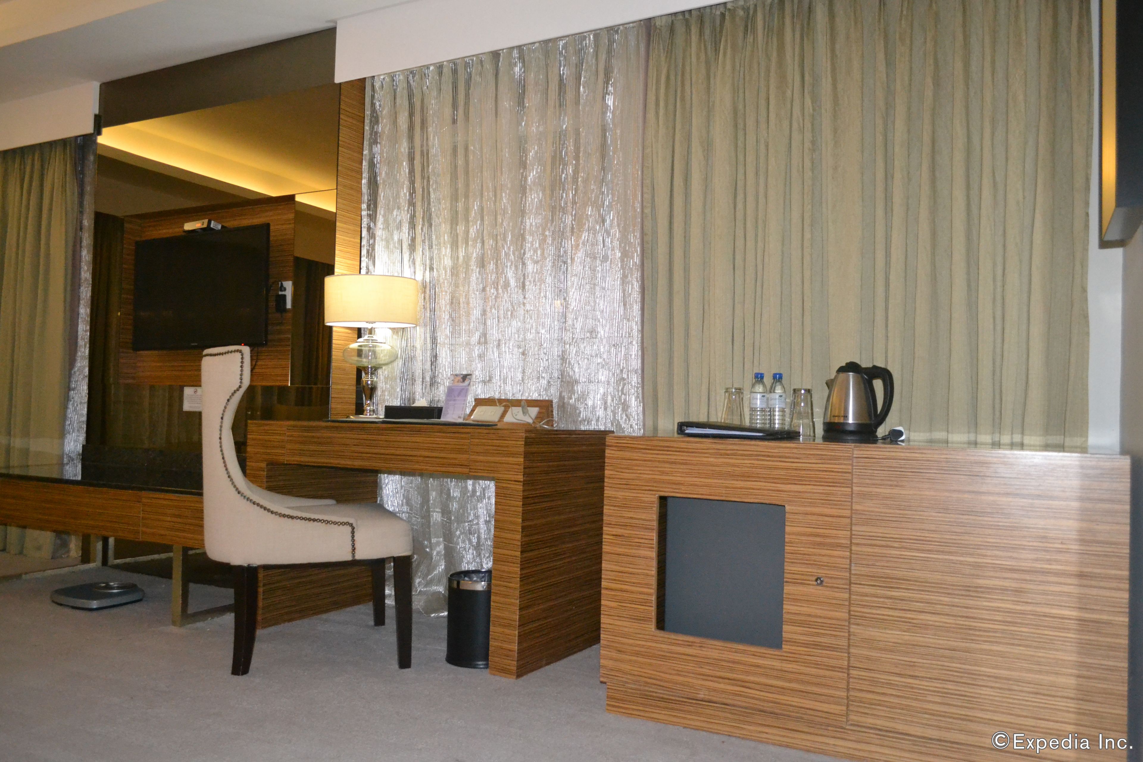 A hotel room with a wooden desk, a chair, a television, a lamp, and a minibar.