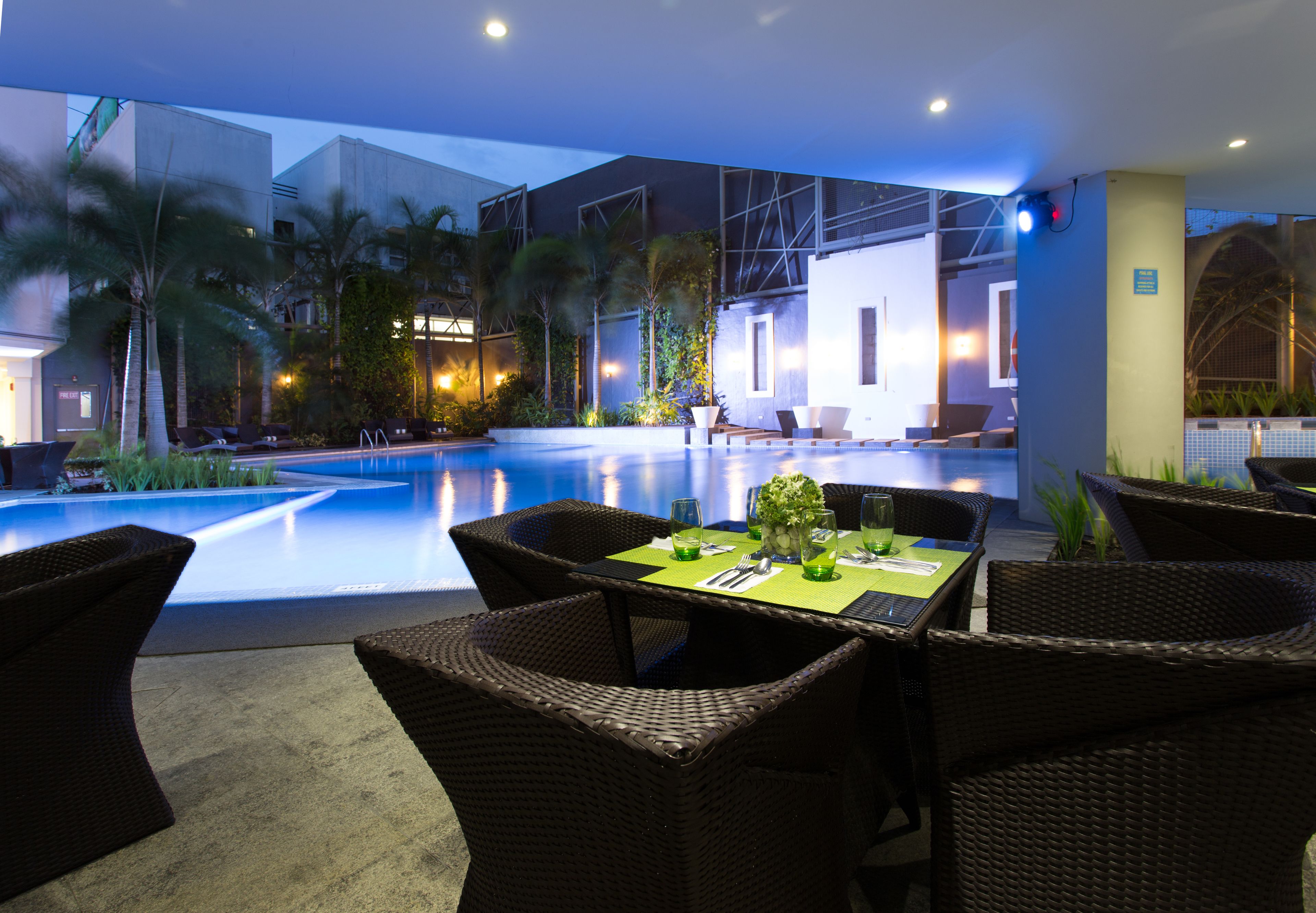 Un área de comedor junto a la piscina con muebles de mimbre y una mesa preparada para dos.